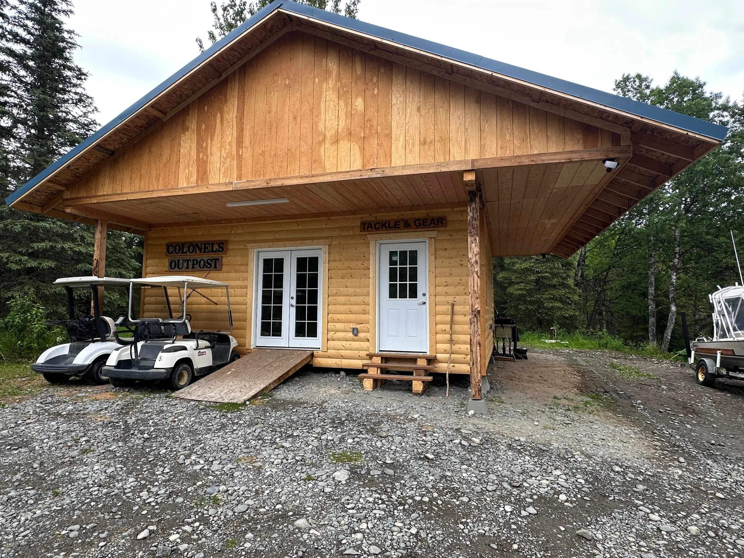 Colonel's Outpost by day, golden log siding under the big gable, both signs, carts parked under the eave