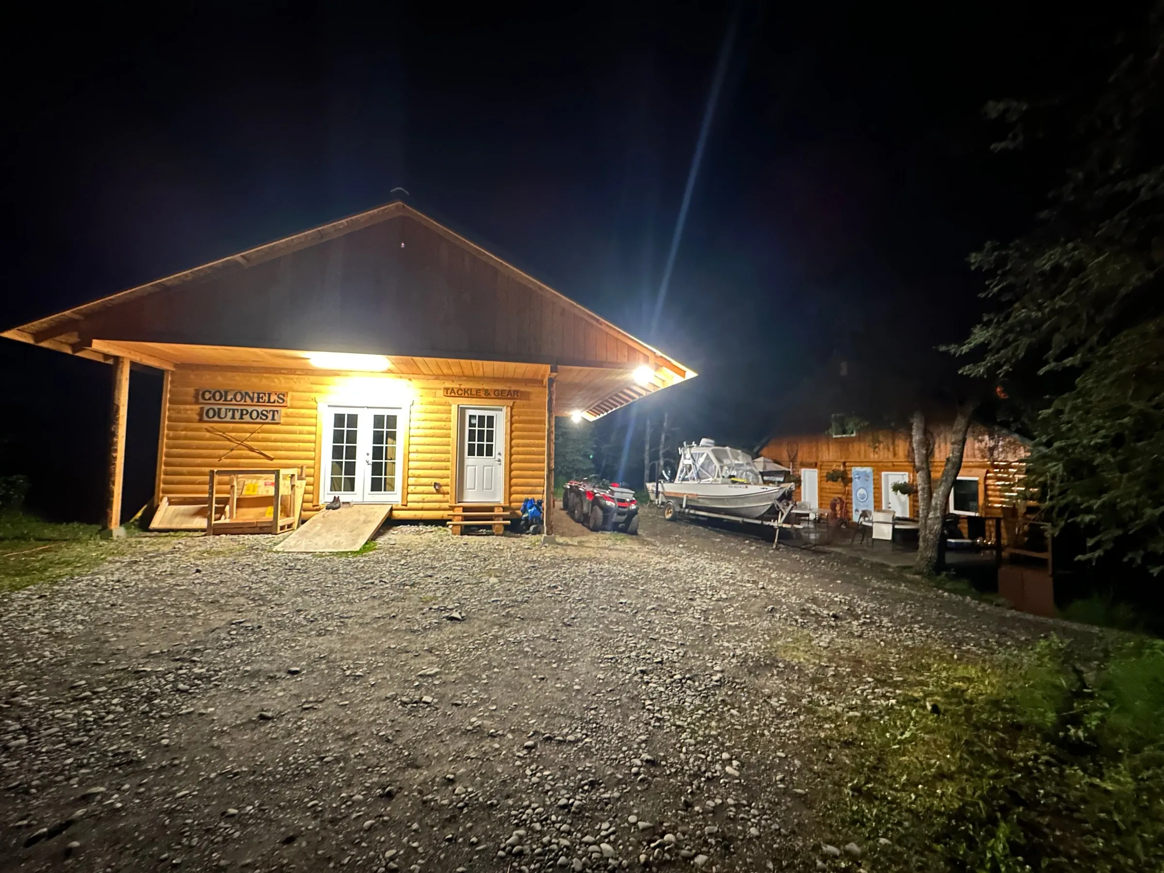 Colonel's Outpost lit up warm at night, the charter boat parked alongside and spruce all around