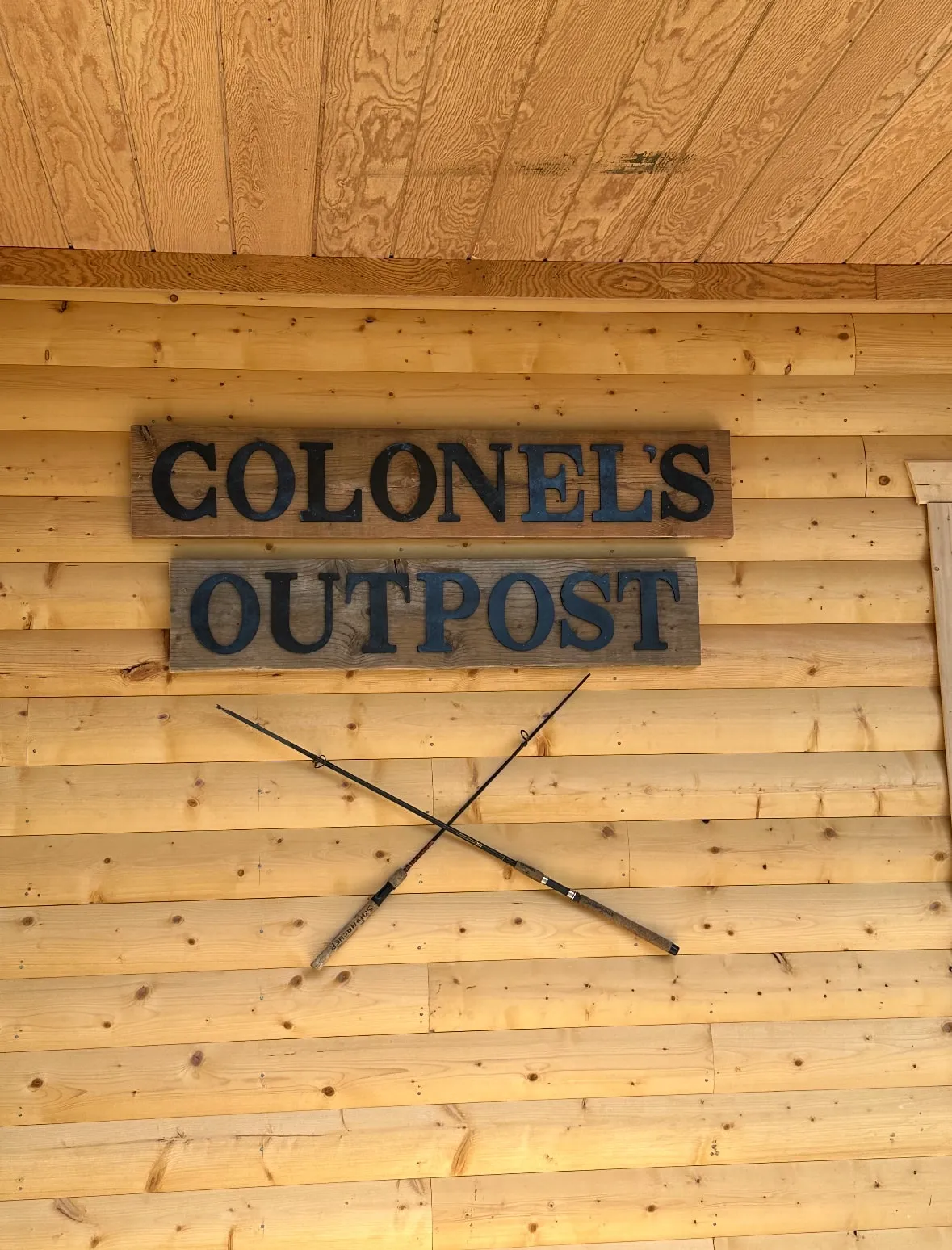 The carved Colonel's Outpost sign with crossed oars, routed into the log wall