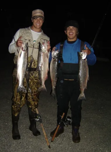Two anglers holding up a pair of large salmon on the dock.