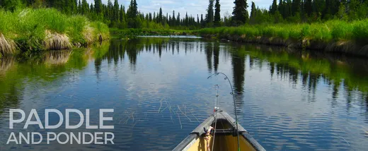 Calm river reflection with mountains and spruce trees in the distance.