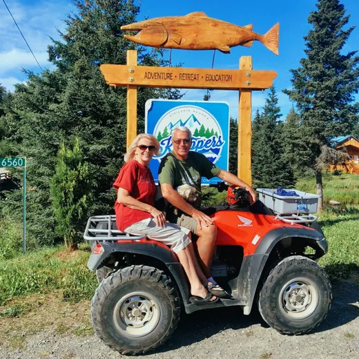 Guests on a red ATV near a carved wooden fishcamp entrance sign