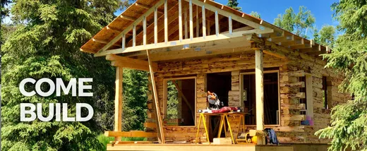 'Come Build' — log cabin construction in progress, walls going up