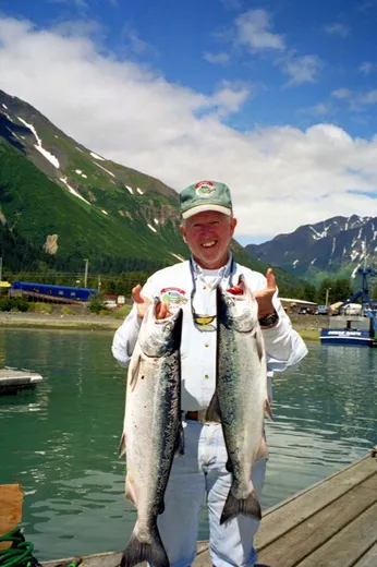 Guest holds two large salmon with mountains behind.