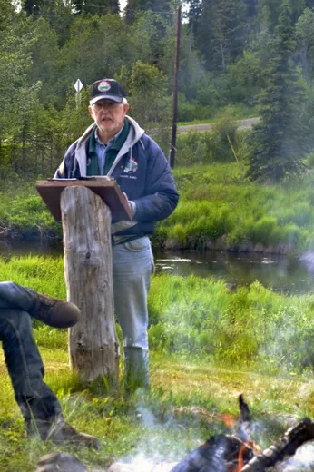 Angler stands streamside holding a large salmon catch.