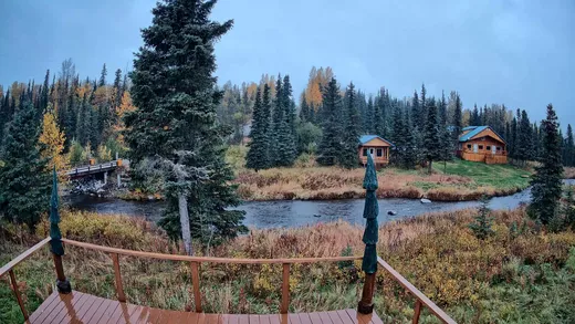 Overcast sky over a fenced meadow with spruce trees at dusk.